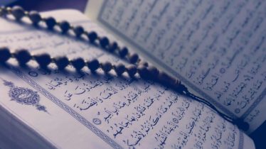 A close-up of prayer beads resting on an open Quran page, depicting Islamic faith and worship.