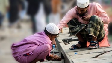 A father and son share a moment beside a small stream, both wearing traditional attire.