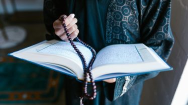 A woman in traditional attire reads a holy book with prayer beads, symbolizing faith and devotion.
